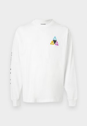 Balta krekls ar garām piedurknēm un mazu trīsstūrveida logotipu zilā, dzeltenā, melnā un rozā krāsā kreisajā krūtīs, kā arī melnu tekstu uz labās piedurknes.