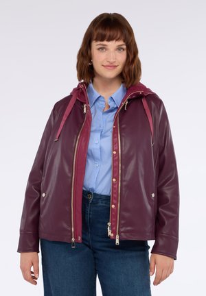 Veste en simili cuir bordeaux avec capuche, fermeture éclair à l'avant et boutons-pression. Présente une finition brillante et deux poches latérales. Portée par-dessus une chemise bleue.