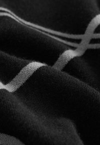 Tissu noir doux avec une surface texturée et des lignes blanches courbes formant une partie d'un motif sur le tissu.