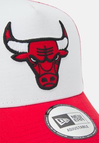Gorra de béisbol roja y blanca con un logo de toro bordado en la parte delantera. Cierre ajustable tipo snapback. La tela tiene una textura suave.