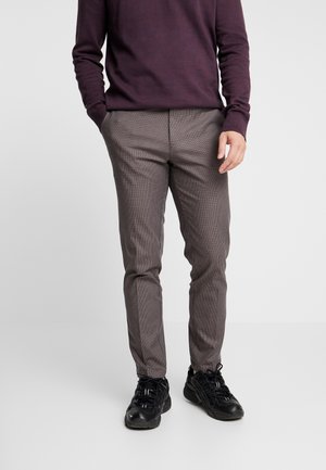 Pantalones de cuadros grises con un ajuste entallado, bolsillos laterales visibles y una textura sutil, combinados con zapatillas deportivas negras.