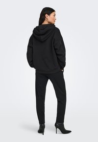 Sudadera negra de gran tamaño con capucha, combinada con pantalones negros de corte entallado. La tela parece suave; la modelo lleva botas negras de tacón alto.