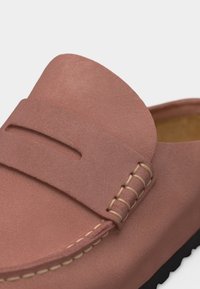 Κοντινό πλάνο απαλού ροζ μοκασίνι από σουέντ με ραμμένες λεπτομέρειες και μαύρη λωρίδα από καουτσούκ κατά μήκος της σόλας.