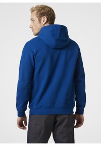Sudadera azul con una gran capucha, tela texturizada, mangas largas y dobladillo acanalado. Combinada con pantalones oscuros, presenta un ajuste relajado desde la parte trasera.