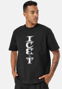 Černé bavlněné tričko s vertikálním bílým textem „ICE T“ ve výrazném, stylizovaném písmu. Krátké rukávy a kulatý výstřih.