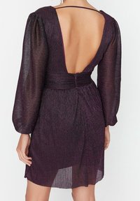 Głęboki fioletowy sukienka z długimi, przezroczystymi rękawami, odkrytymi plecami i marszczonym stanikiem. Teksturowana tkanina z subtelnym połyskiem. Krótka długość.