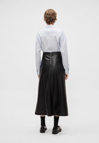 Fekete bőr midi szoknya hátul cipzáras záródással. Világoskék hosszú ujjú inggel és fekete zoknival párosítva.