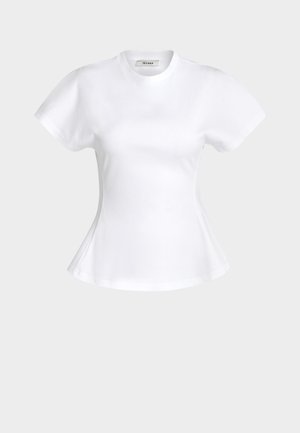 Kvinne iført en hvit kortermet tettsittende topp, svarte vide bukser, svarte spisse sko, et halskjede, og holder en brun håndveske.