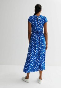 Abito blu con pois bianchi astratti, maniche a palloncino corte, una fascia in vita e un design fino al ginocchio con apertura a chiave sul retro. Sneakers bianche.