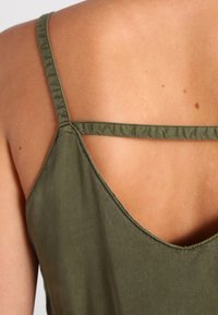 Olivově zelený bezrukávový top s tenkými ramínky, s kulatým výstřihem na zádech. Hladký povrch s jednoduchým designem a bez viditelných vzorů či akcentů.
