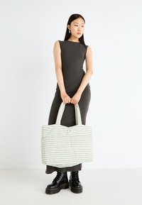 Striped, padded tote bag in light cream with blue and green lines. Features two sturdy handles and a button closure.