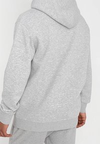 Felpa grigia realizzata in tessuto testurizzato, con cappuccio regolabile tramite cordino, polsini e orlo a coste. La parte posteriore presenta un design semplice e senza decorazioni.