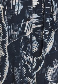 Marinblått tyg med ljusblå och vita abstrakta fjädermönster, med svarta knappar ner genom mitten.