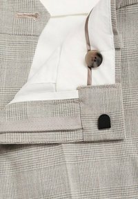 Gråternet stof med en glat hvid foring, der har en brun knap og en sort detalje. Flad, skræddersyet design med rene kanter.