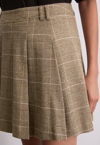 Jupe à carreaux marron avec un design plissé, fabriquée à partir d'un tissu texturé avec une finition lisse et des détails de taille cousus.
