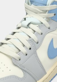 Zbliżenie białego i jasnoniebieskiego sportowego buta z białymi sznurówkami przewleczonymi przez oczka na górnej części.