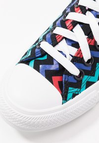 Bunte Segeltuchschuhe mit einem schwarzen Zickzackmuster in Blau, Rot und Türkis, mit einer weißen Gummikappe und Schnürsenkeln.