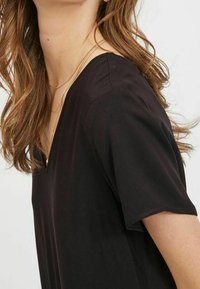 Svart V-ringad topp med korta ärmar, slät tyg, avslappnad passform, subtil lyster och en enkel design utan mönster eller dekorationer.