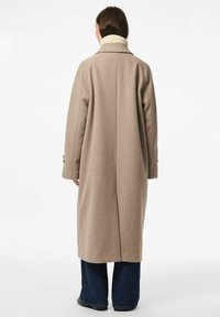 Cappotto di lana beige con colletto alto, taglio dritto e tasche laterali, con una cucitura centrale lungo la schiena e polsini abbottonati.