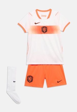 Λευκή και πορτοκαλί ποδοσφαιρική εμφάνιση με το έμβλημα του λιονταριού της Ολλανδίας, λογότυπα Nike και ταιριαστό λευκό κάλτσα, τοποθετημένη επίπεδα σε λευκό φόντο.