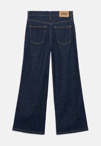 Jeans de mezclilla oscura de pierna ancha con cintura alta, cinco bolsillos, etiqueta de cuero marrón en la parte trasera y detalles de costura en contraste.