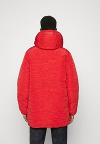 Rode gewatteerde jas met een capuchon, textuurstof met een subtiel reliëfpatroon en elastische manchetten, getoond vanaf de achterkant.