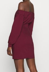Bordeaux rotes Off-Shoulder-Kleid mit langen Puffärmeln, tailliertem Oberteil und glatter Textur. Reißverschluss hinten, knielanger Saum.