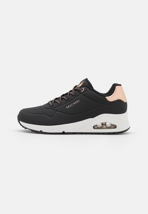 Zwarte lage Skechers sneaker met witte zool, roségouden hielaccent, zwart-witte veters en zichtbaar luchtkussen in de zijkant van de zool.