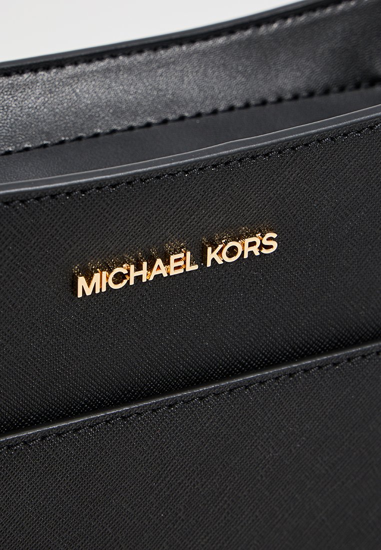Schwarze Stoffhandtasche mit strukturiertem Oberflächen, ausgestattet mit einem goldenen "MICHAEL KORS"-Logo und eleganten Kanten. Schlichtes, funktionales Design.
