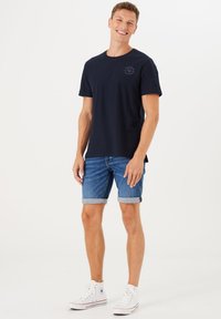 Navy katoenen t-shirt met een ronde halslijn, gecombineerd met opgerolde denim shorts. Witte hoge sneakers maken de outfit af. Eenvoudig en casual ontwerp.