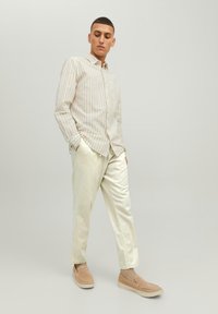 Striped beige button-up shirt, light cream trousers, and beige slip-on shoes. Smooth fabric with a relaxed fit and minimal detailing.
