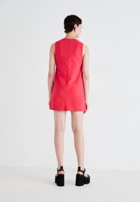 Red sleeveless dress with a high neckline, fitted design, and back seam detail, paired with chunky black platform sandals.