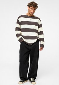 Bruine en crème gestreepte lange mouw shirt, gestructureerde stof, losse pasvorm. Combinatie met zwarte wijde broek en zwarte sneakers met witte accenten.