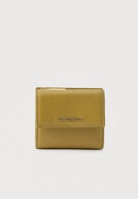 Billetera compacta de cuero texturizado en color verde oliva con solapa y logo plateado de COCCINELLE en la parte frontal, situada sobre un fondo claro y liso.