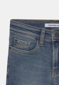 Džínové kalhoty Calvin Klein v středně modré barvě. Design s pěti kapsami, kontrastní prošití, logo na kapsičce a kovové zapínání na knoflík.
