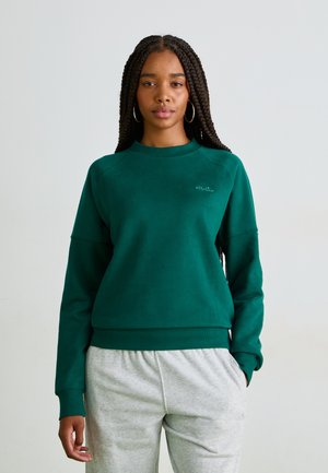 Sweat-shirt vert à col rond fabriqué dans un matériau doux, avec des poignets et un ourlet côtelés. Associé à un pantalon de survêtement gris clair, arborant un branding discret.