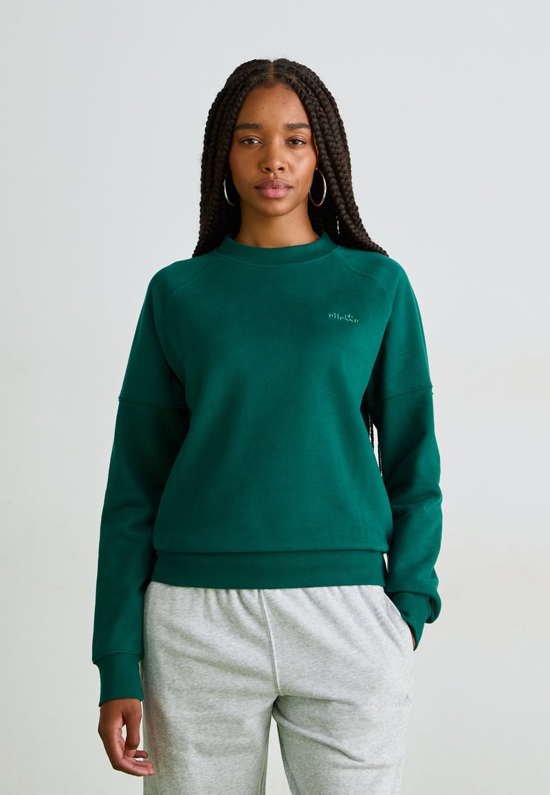 Sudadera verde de cuello redondo hecha de un material suave, con puños y dobladillo acanalados. Combinada con pantalones de chándal gris claro, que presentan una marca sutil.