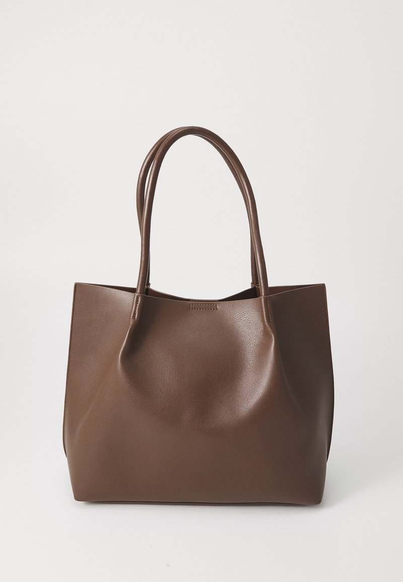 Sac cabas en cuir marron avec deux longues poignées, texture lisse et un design simple et épuré sur fond blanc uni.