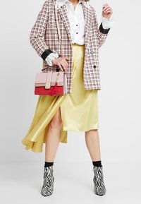 Marynarka w kratę, biała koszula z falbanami, żółta satynowa spódnica, różowa i czerwona torebka oraz botki w paski zebry. Teksturowany i warstwowy design.