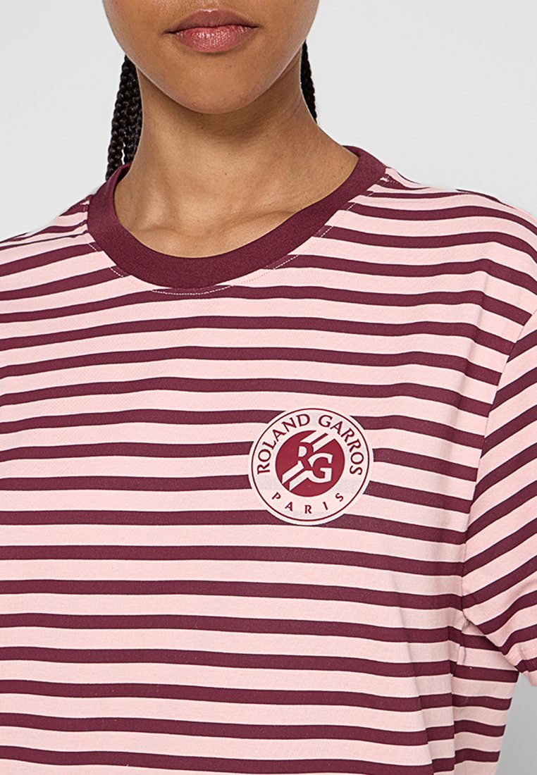 Camiseta a rayas en color marrón y rosa claro con cuello redondo y un parche de logo que presenta "Roland Garros París" en la parte izquierda del pecho.
