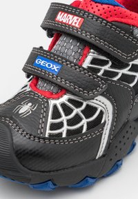 Sneaker nere e rosse con pannelli in rete, con un design a ragnatela, cinturini in velcro e dettagli blu sulla suola. Dettagli del logo sui cinturini.