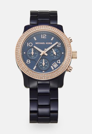 Montre Michael Kors bleu marine avec lunette en or rose sertie de cristaux, trois sous-cadrans, fenêtre de date à 4 heures, et bracelet à maillons.