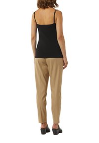 Top nero senza maniche con spalline sottili, abbinato a pantaloni beige chiaro di sartoria. Footwear con tacco largo e design aperto sul retro.