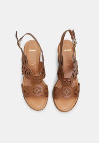 Sandales en cuir marron avec un design floral découpé, bride de cheville réglable et semelle rembourrée. Détails de la couture sur les bords.
