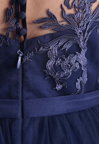 Námořnická modrá šaty s propracovanou květinovou výšivkou, průhledným síťovým živůtkem, strukturovanou tkaninou a zapínáním na zip se zdobnými knoflíky.