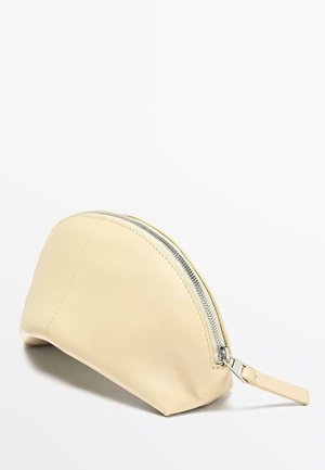 Beżowa skórzana kosmetyczka w kształcie półksiężyca, z srebrnym zamkiem i małym paskiem. Gładka faktura i minimalistyczny design.
