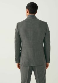 Gray houndstooth blazer with a structured design, peak lapels, and button accents, paired with matching pants, viewed from the back.