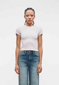 Ανοιχτό ροζ κοντομάνικο μπλουζάκι από μαλακό ύφασμα. Συνδυασμένο με ψηλόμεσα, ξεθωριασμένα μπλε τζιν παντελόνια.