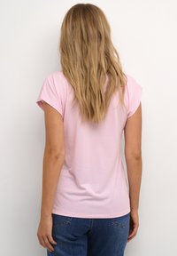 T-shirt rose clair à manches courtes en tissu doux, avec un col arrondi et une coupe ajustée, associé à un jean bleu.