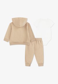 Sweat à capuche beige avec capuche, joggers beige assortis, et body à manches courtes blanc, tous fabriqués en tissu doux avec des détails élastiques.